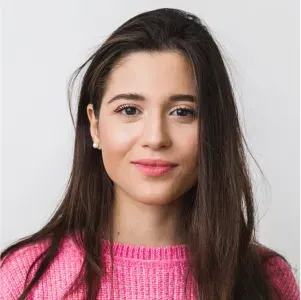 A woman with long hair is wearing a pink sweater and smiling.