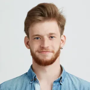 A young man with a beard is wearing a denim shirt and earrings.