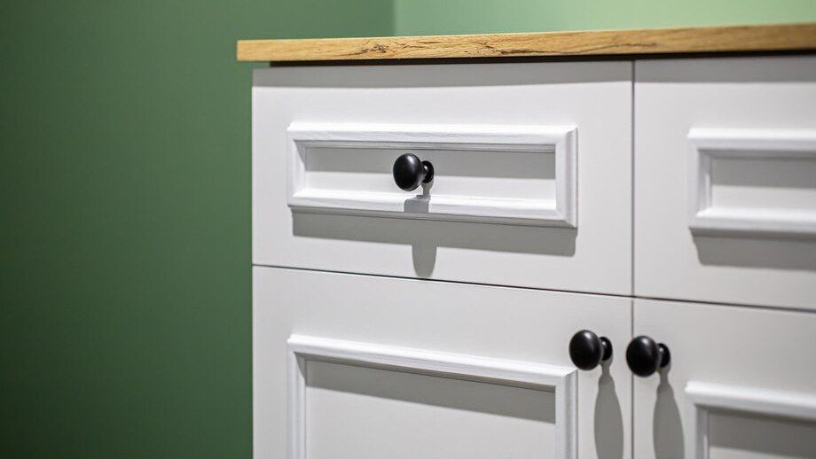 A white cabinet with black handles and a wooden top.