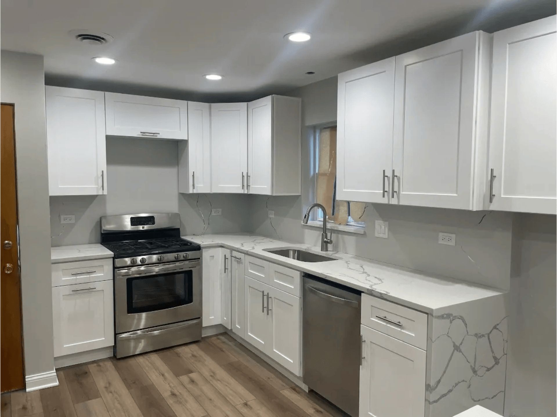 White kitchen with stainless steel appliances, light countertops, and wooden floors.