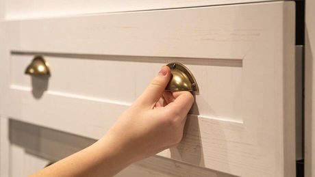 A person is reaching for a drawer handle on a white cabinet.