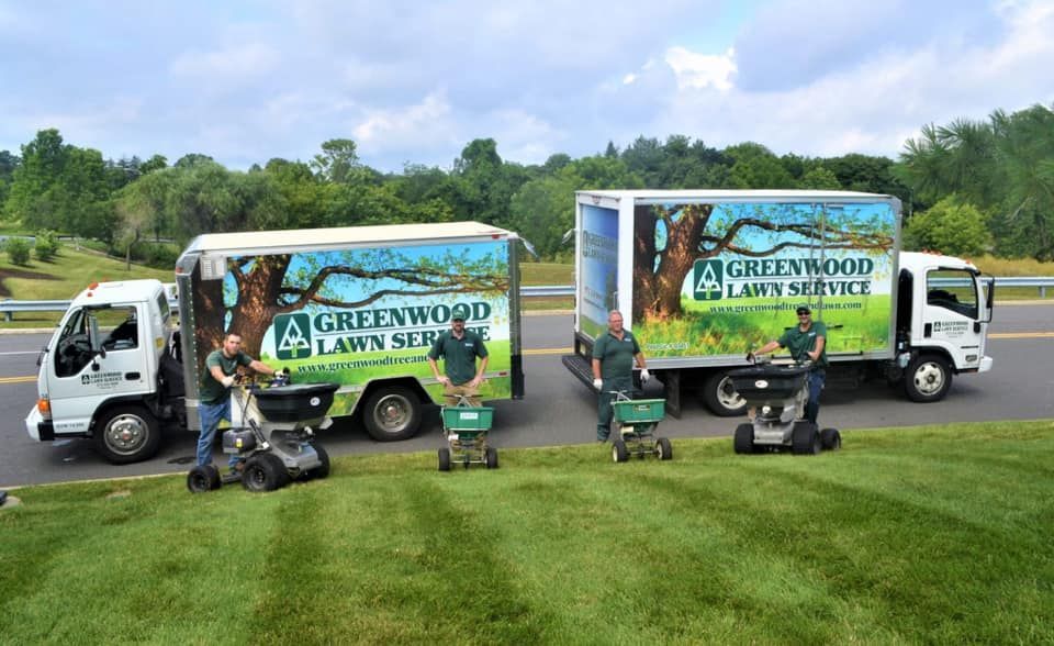 Three greenwood lawn service trucks are parked on the side of the road.