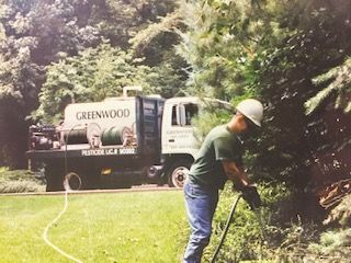 A man is spraying a tree in front of a greenwood truck.