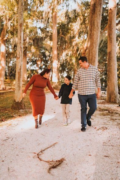 A family is walking down a path in the woods holding hands.