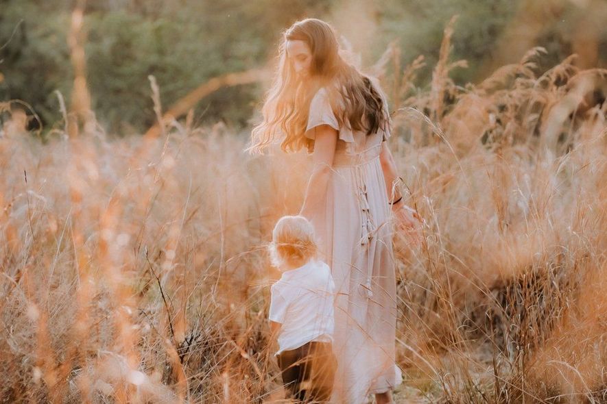 A woman and a child are standing in a field holding hands.