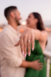 A man is holding a woman 's hand while she shows off her engagement ring.