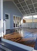 A wooden deck with a covered porch and white trim, leading to a blue house with windows.
