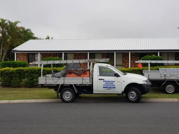 White pickup truck with ladders parked in front of a house, advertising roofing services.