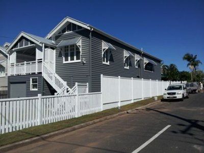 Gray house with white trim, awnings, and fence on a sunny street.