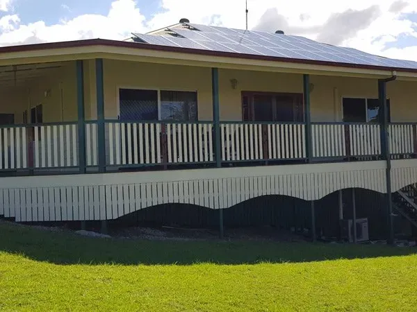 House with solar panels on roof, wrap-around veranda with white railing and green trim.