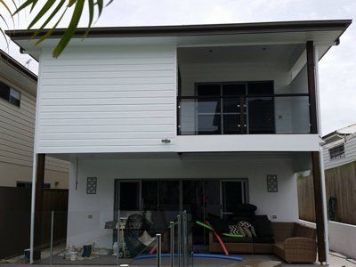Two-story house with white siding and a balcony. Ground level has patio furniture and a pool.