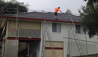 Person on roof, installing scaffolding, two-story house, multiple ladders and scaffolding set up.