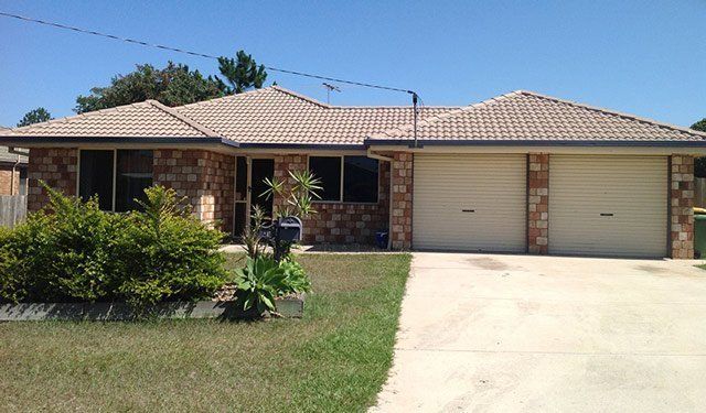 Suburban home with brown tile roof, two-car garage, and a brick facade, under a clear blue sky.