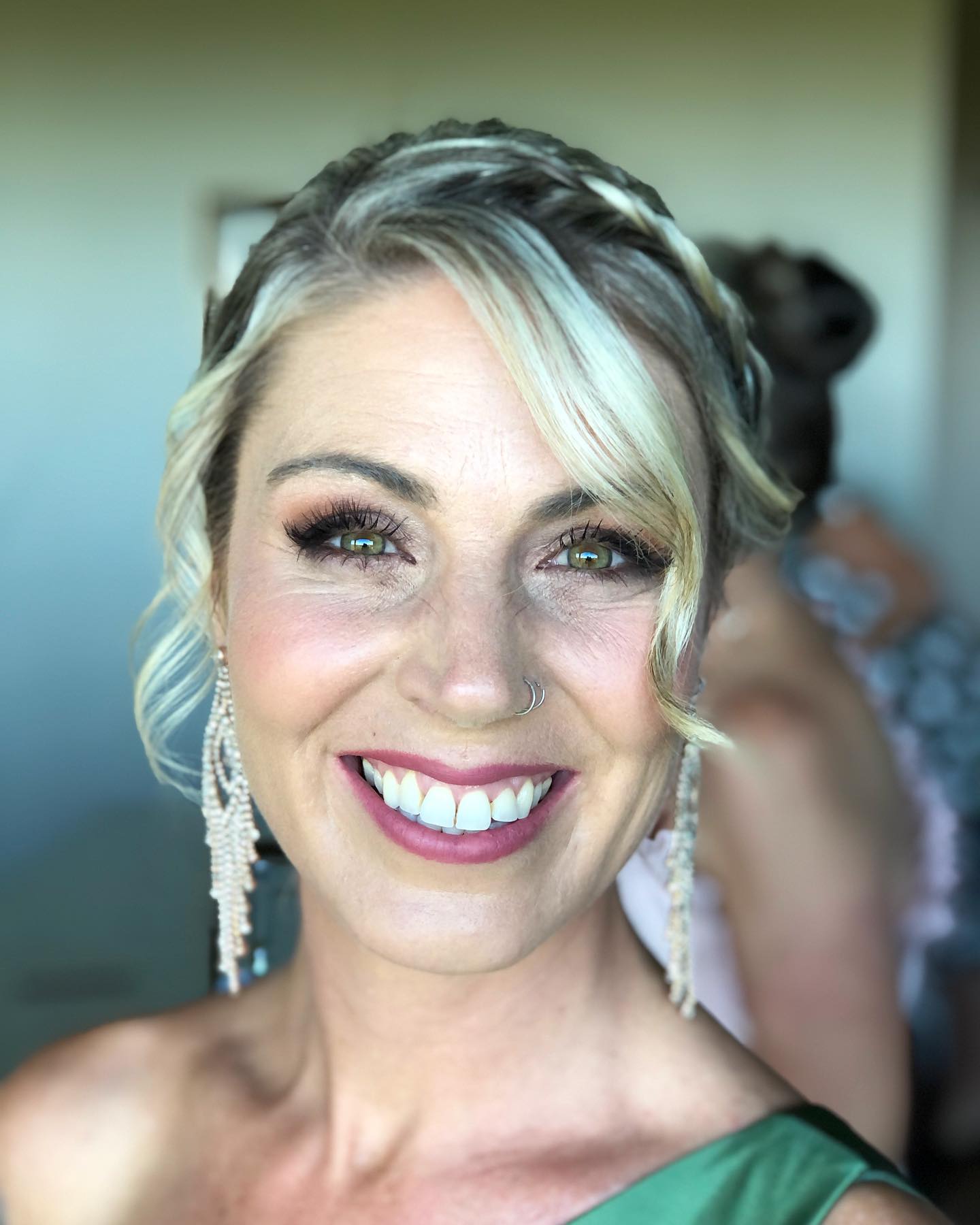 A woman wearing a green dress and earrings is smiling for the camera.