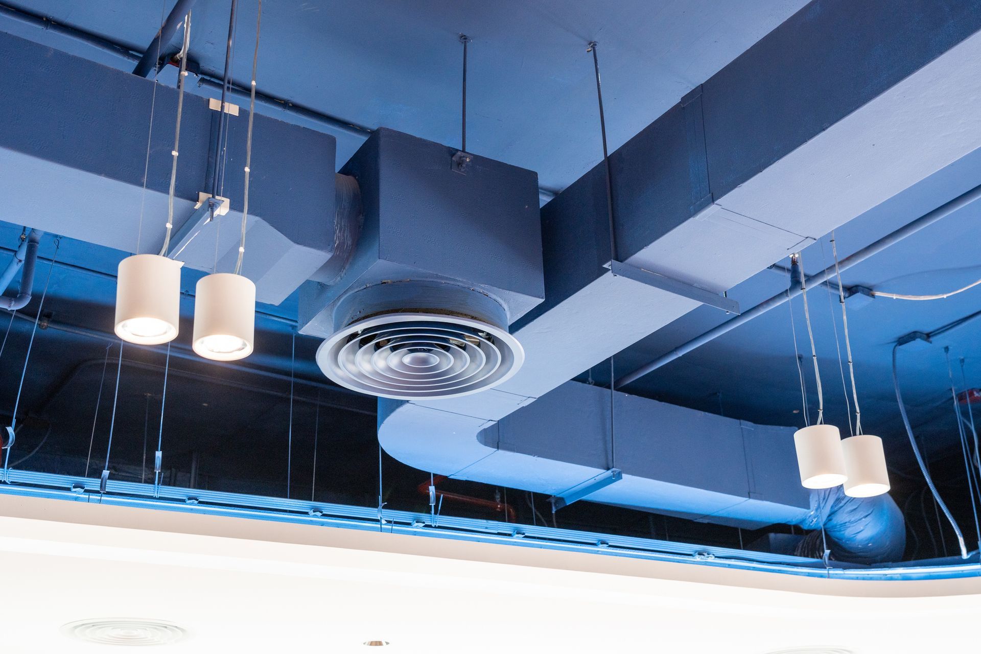 A ceiling with a lot of ducts and lights hanging from it.