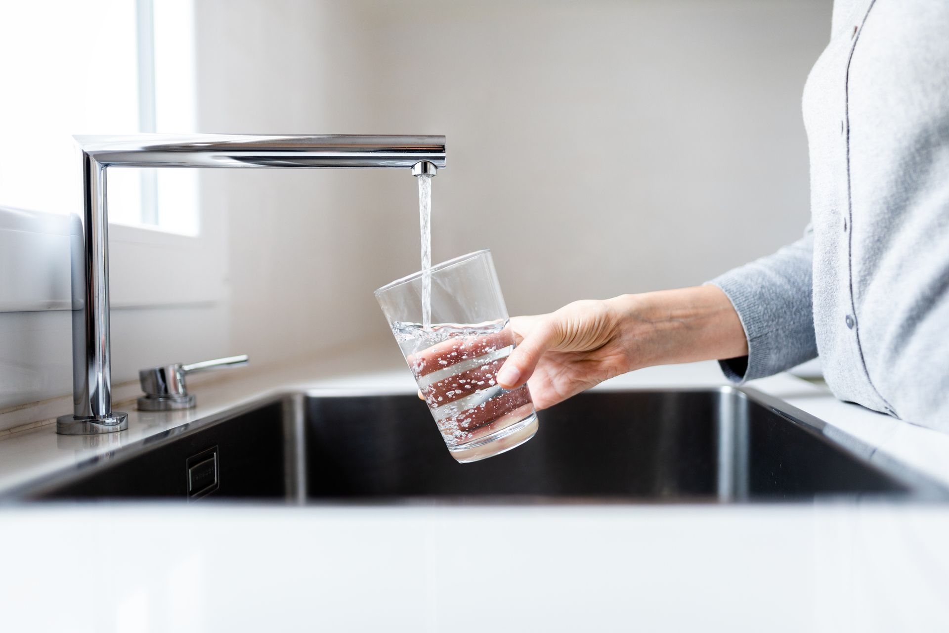 A person is pouring water into a glass from a faucet.
