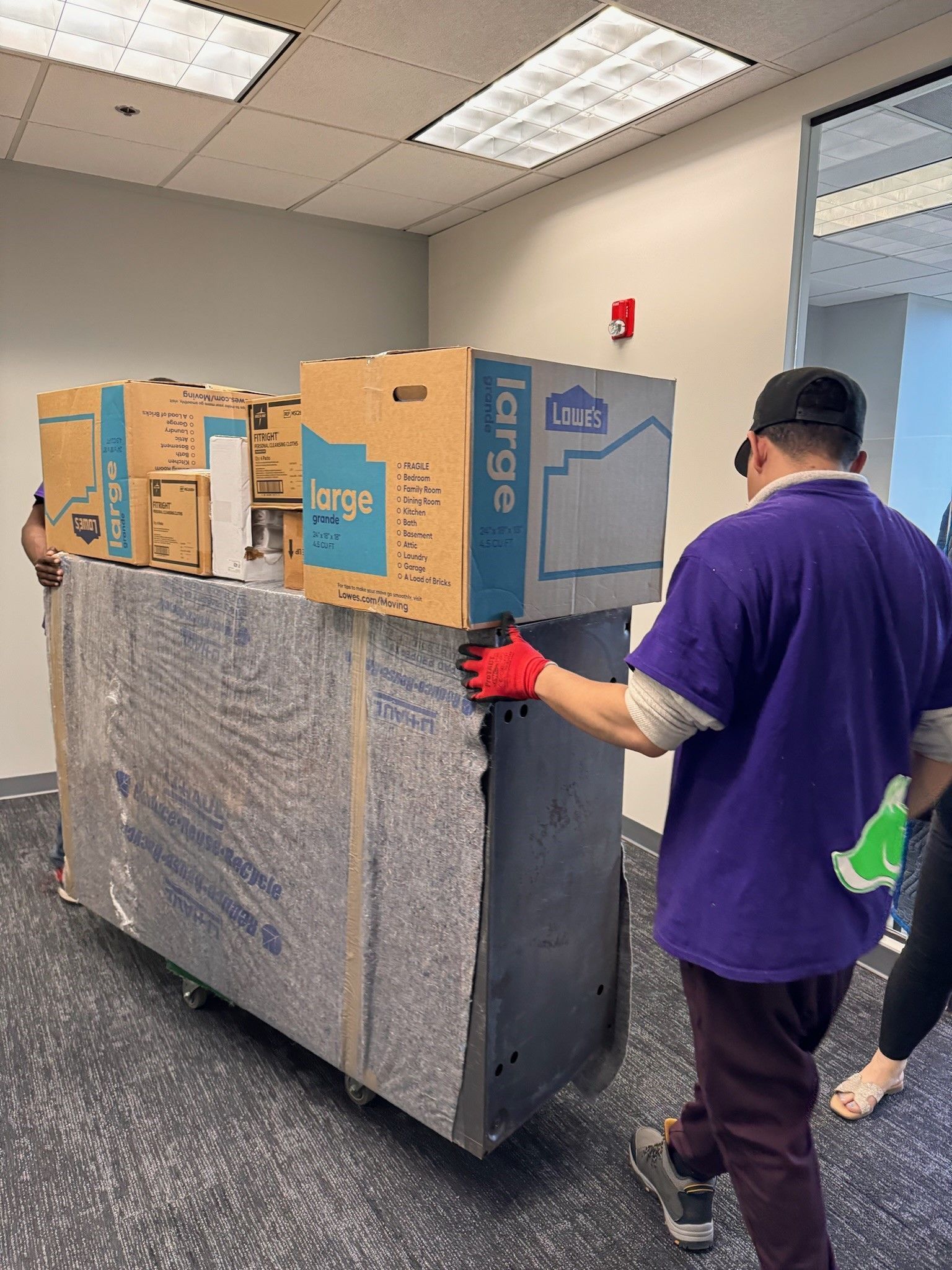 A man in a purple shirt is carrying boxes on a cart.