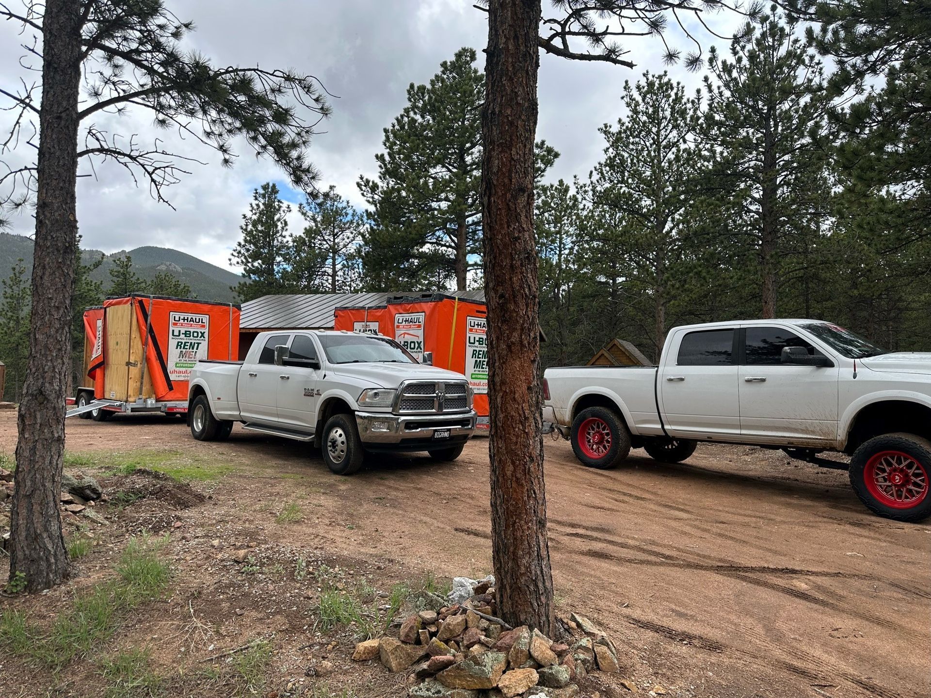 Two white trucks are parked next to each other on a dirt road.