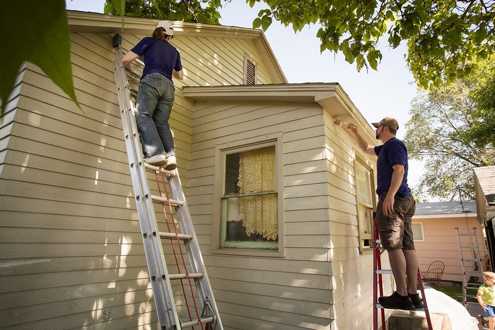 A man on a ladder paints the side of a house
