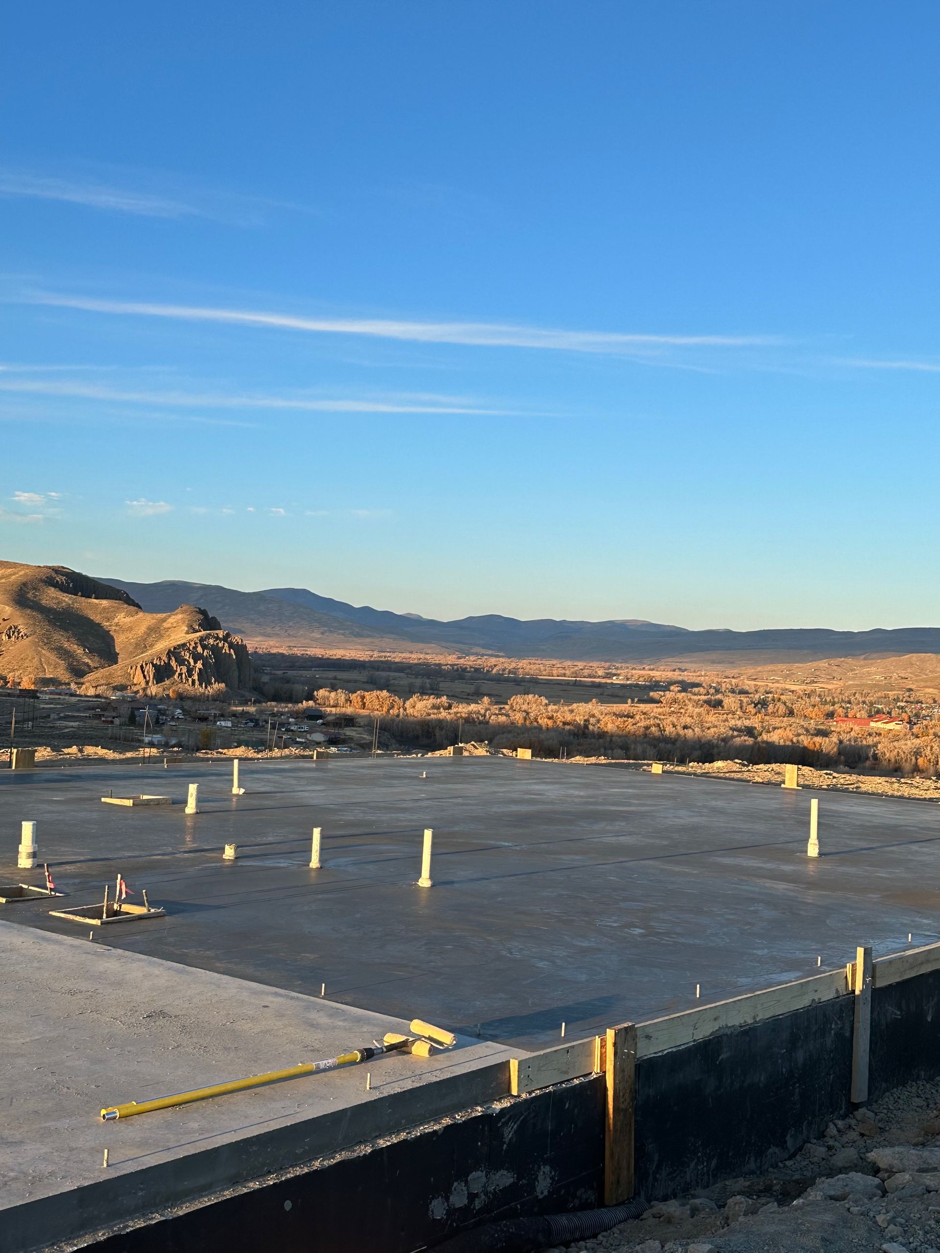 Concrete foundation with plumbing pipes, mountains, and a clear blue sky.
