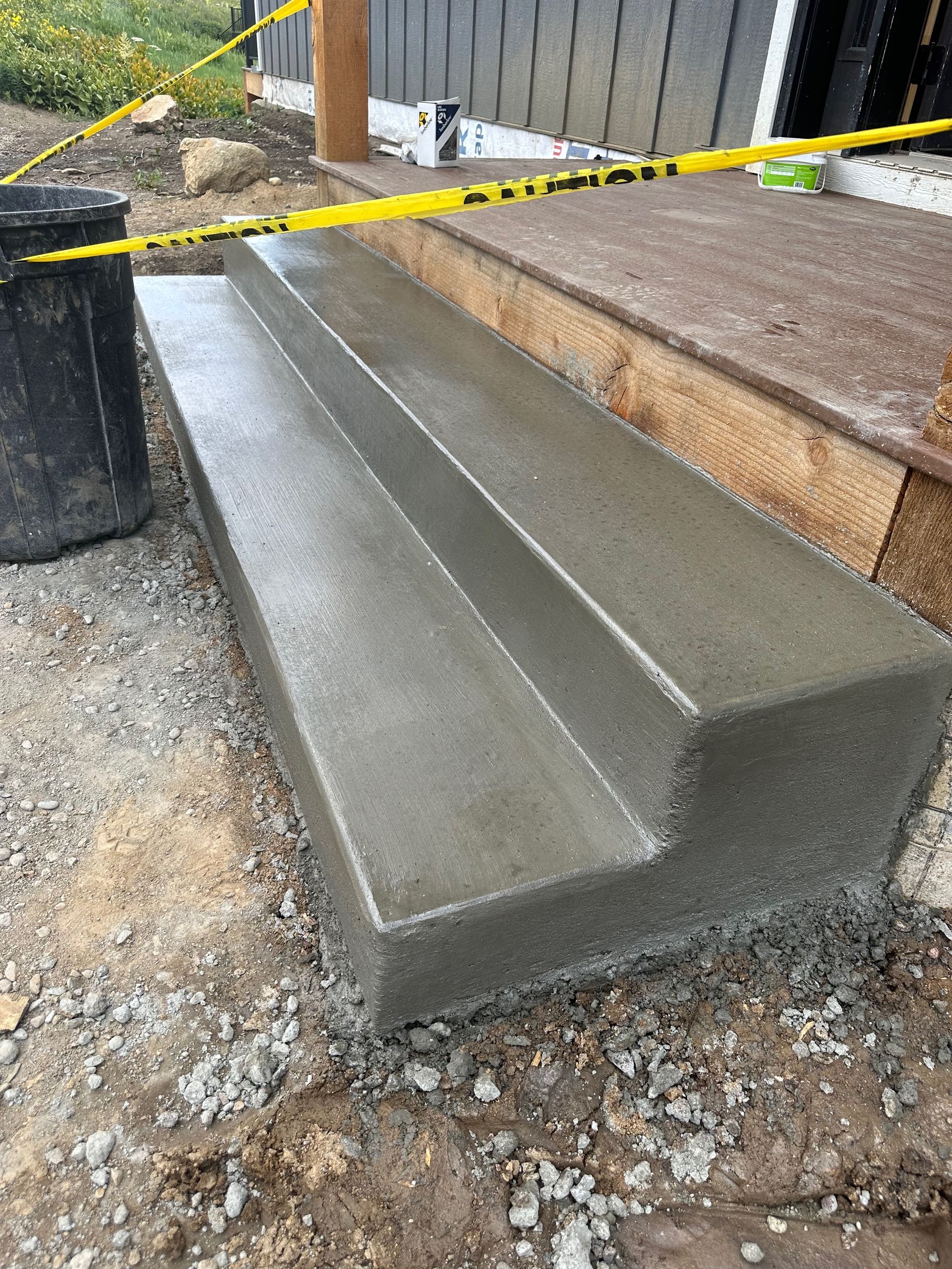 Newly poured concrete steps, wet with a channel, next to a wooden porch.