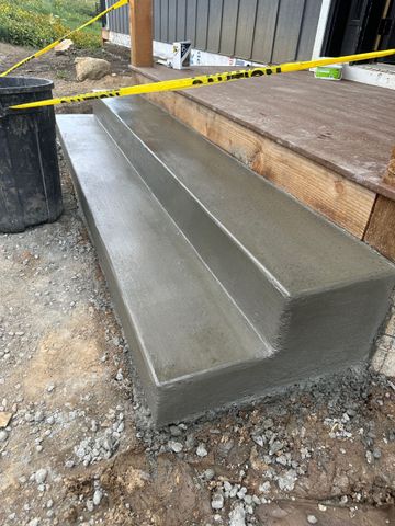 Newly poured concrete steps, wet with a channel, next to a wooden porch.