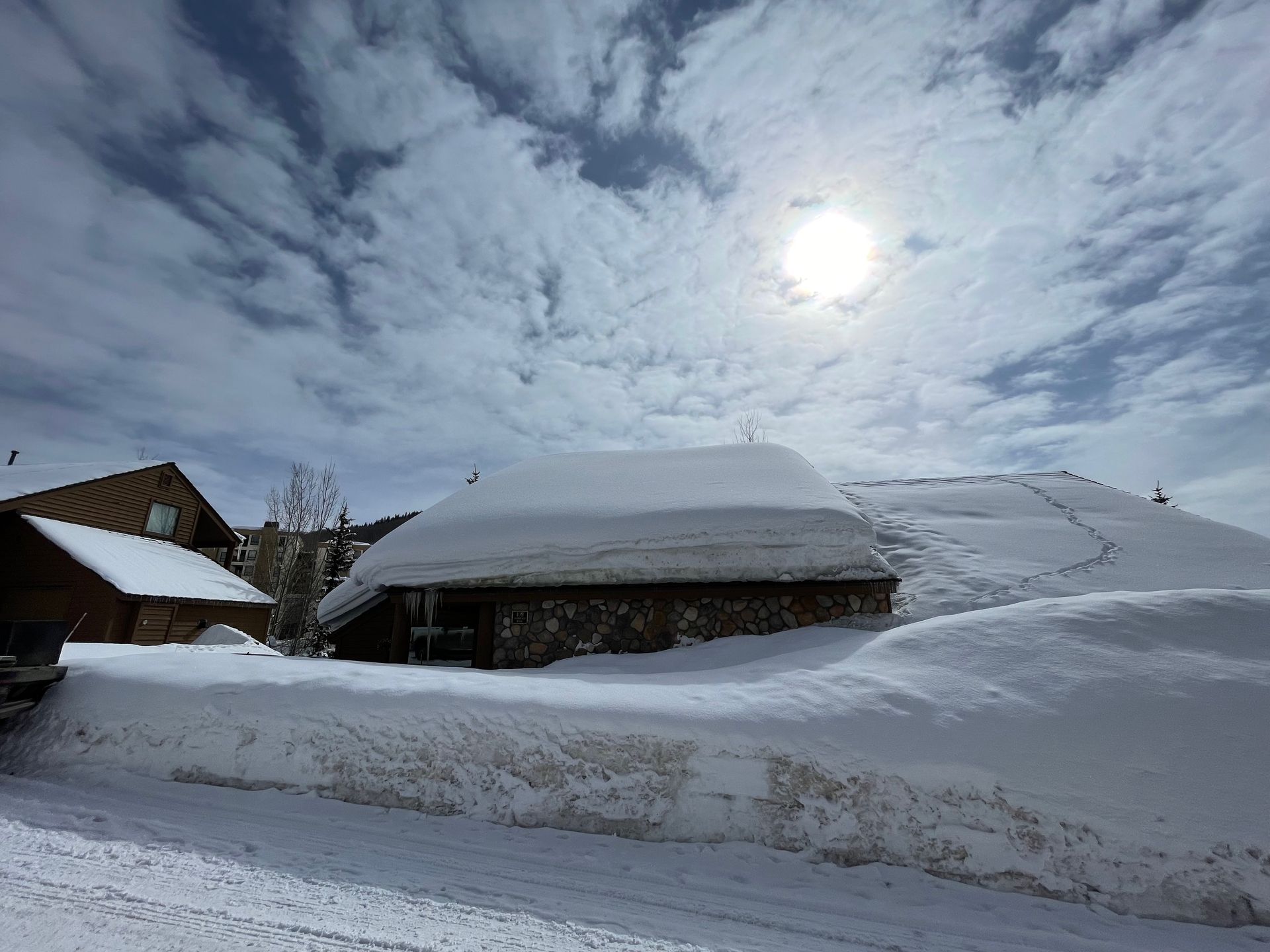 Snow-covered buildings and landscape under a bright sun, with blue sky and clouds.