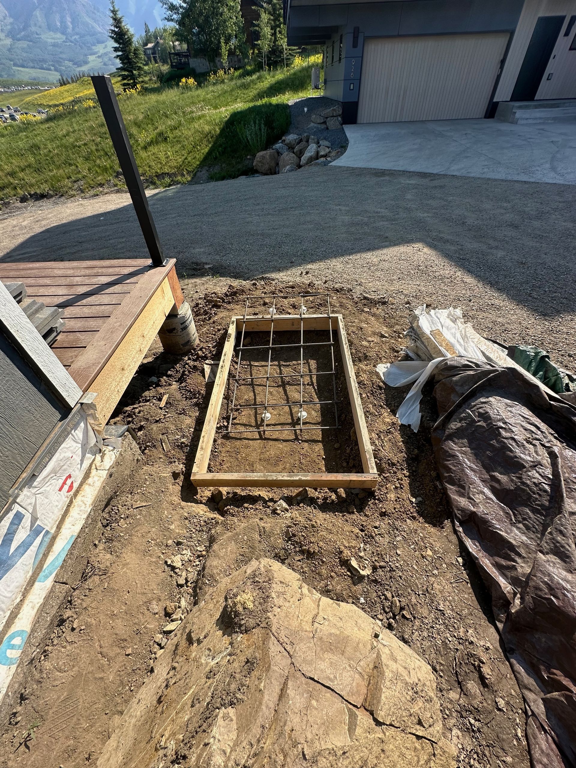 Construction site: rectangular wooden frame with rebar, likely for a concrete step or landing, near a house and driveway.