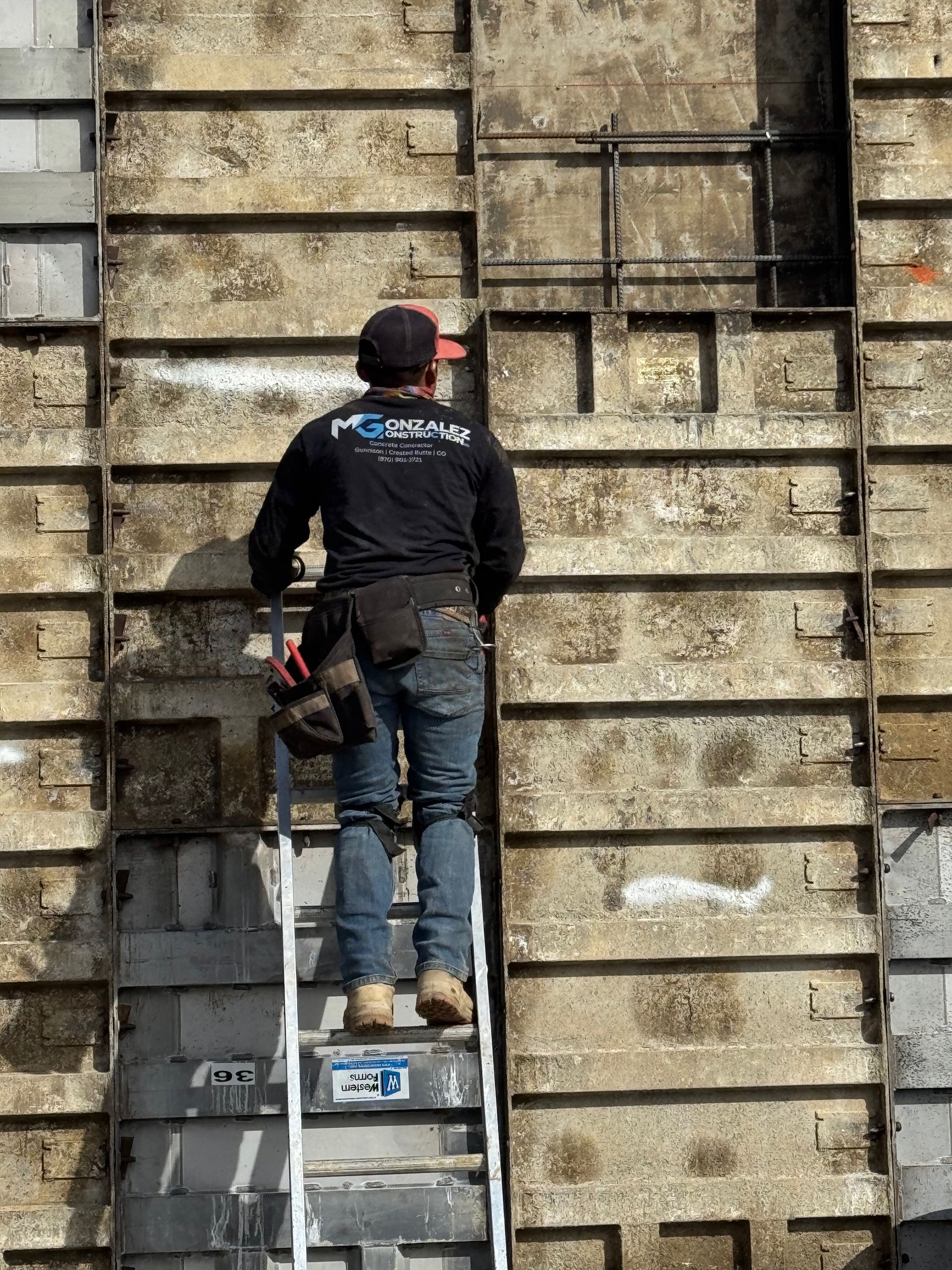 Construction worker on a ladder inspecting a concrete wall with metal framing.