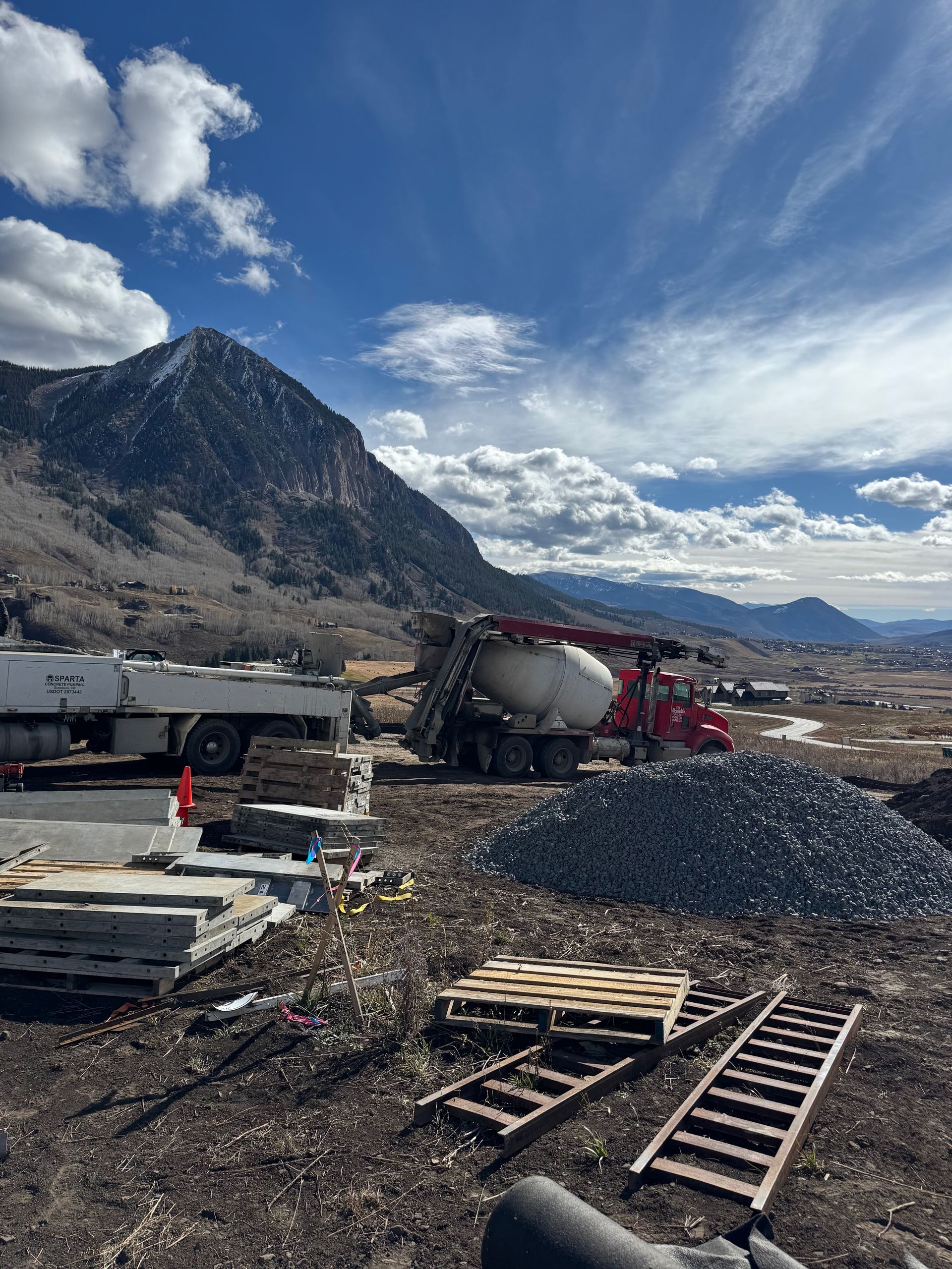 Construction site with a cement truck pouring concrete. Mountain in the background. Sunny, blue sky.