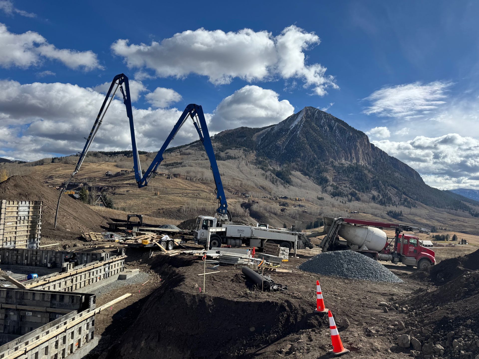Construction site with a concrete pump truck, mountainous backdrop.