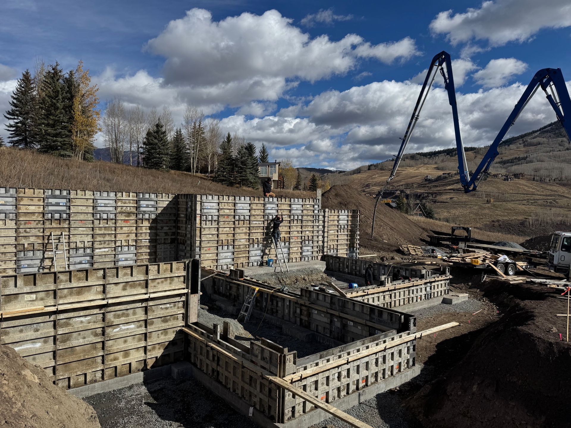 Construction site with wooden forms for concrete walls. Blue sky with clouds, mountains in background.