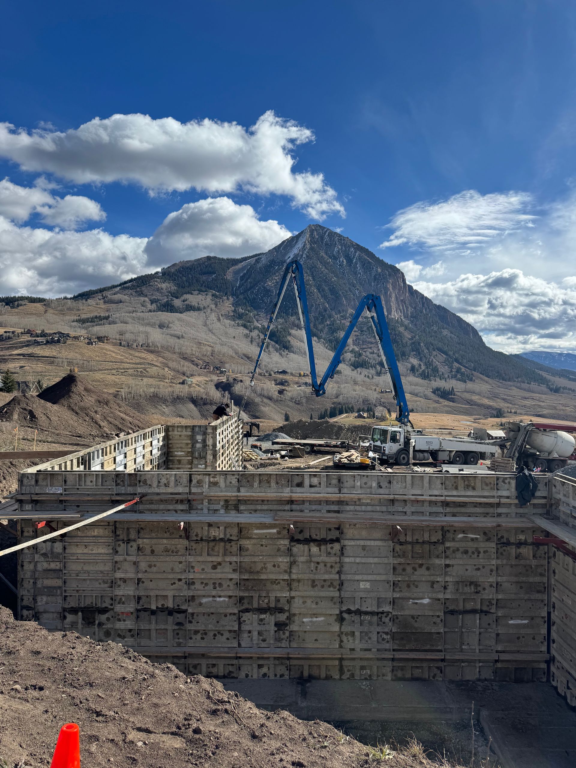 Construction site with a concrete pump pouring concrete, with a mountain backdrop.