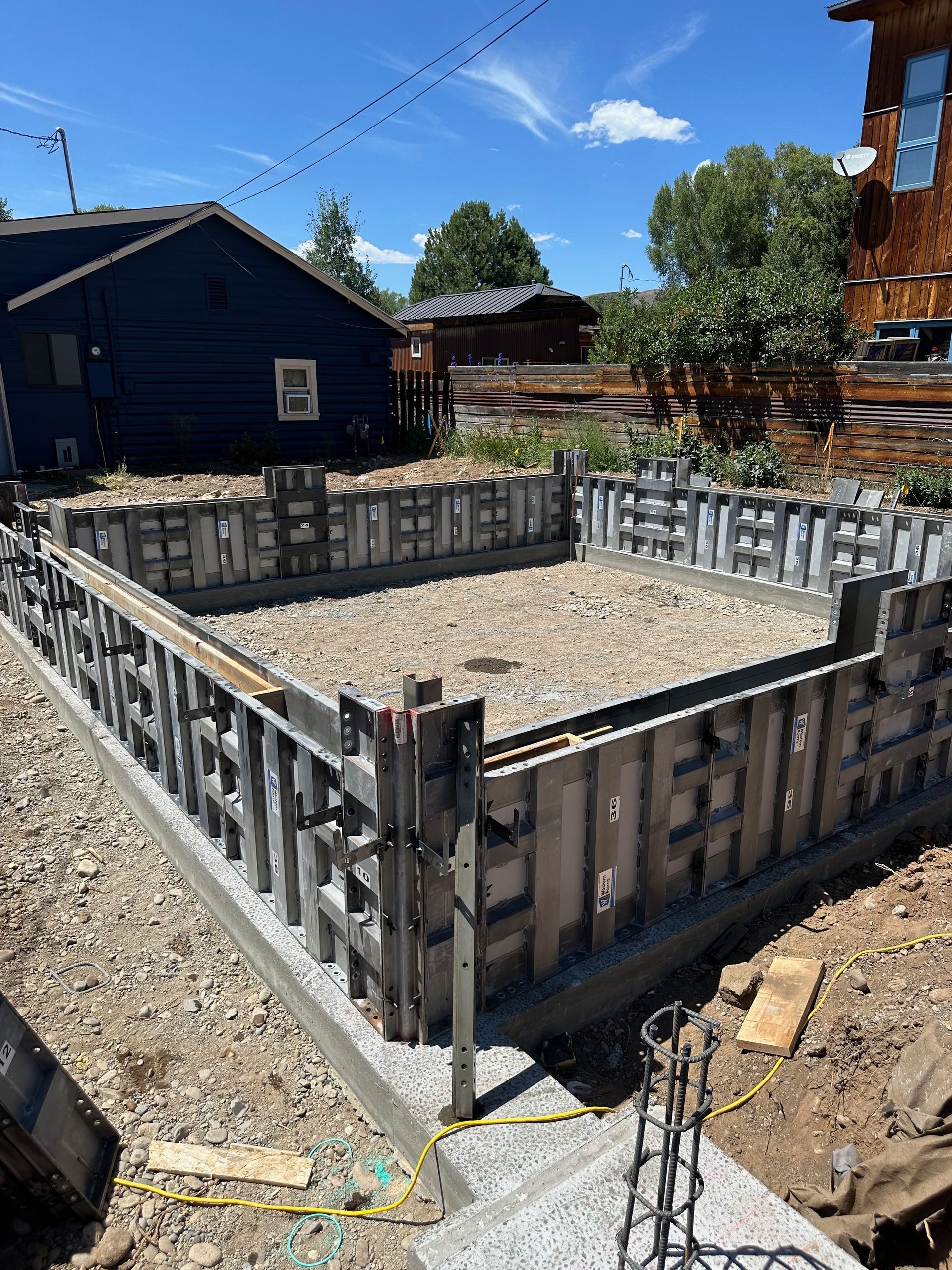 A rectangular concrete foundation with metal framework, prepared for construction, outdoors on a sunny day.