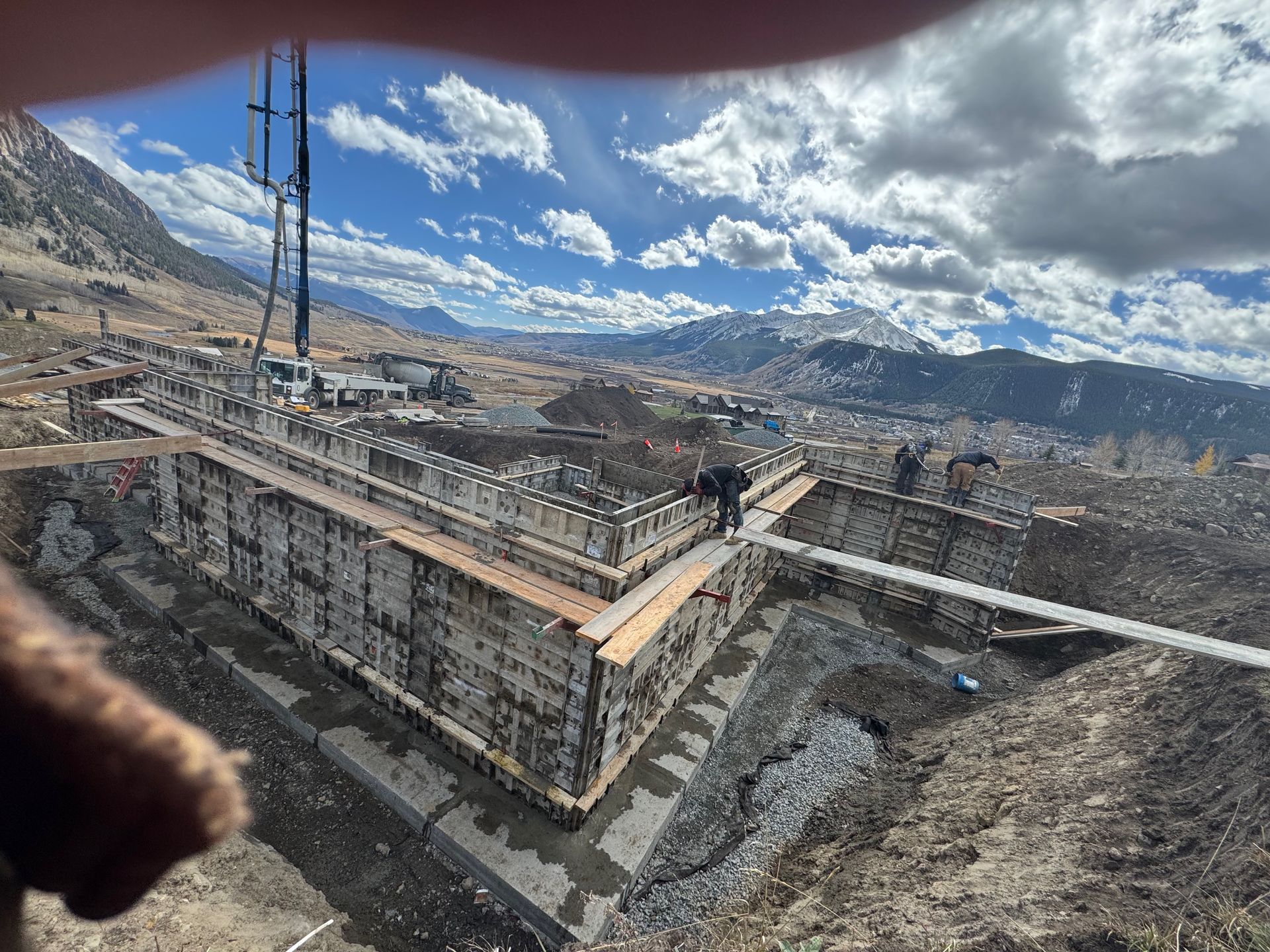 Construction site in mountains, workers on structure, overcast sky.