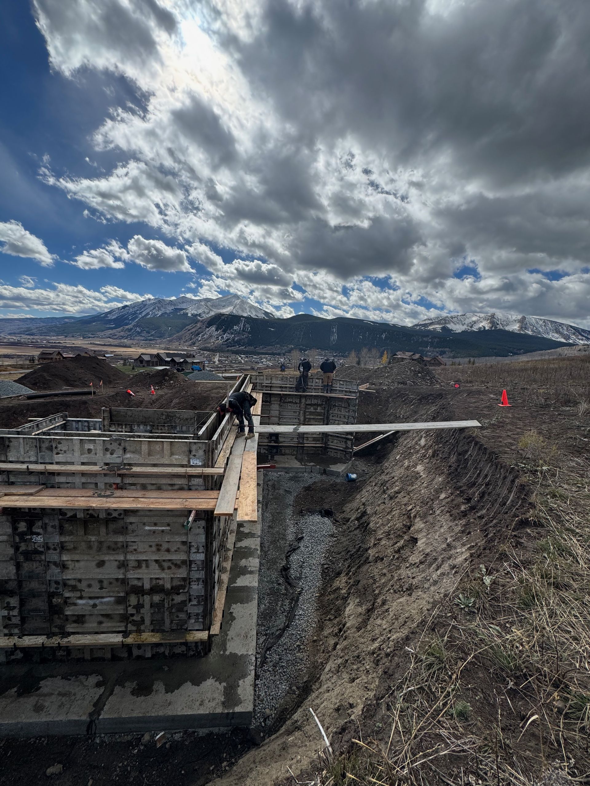 Construction workers on a concrete structure with mountain backdrop and cloudy sky.