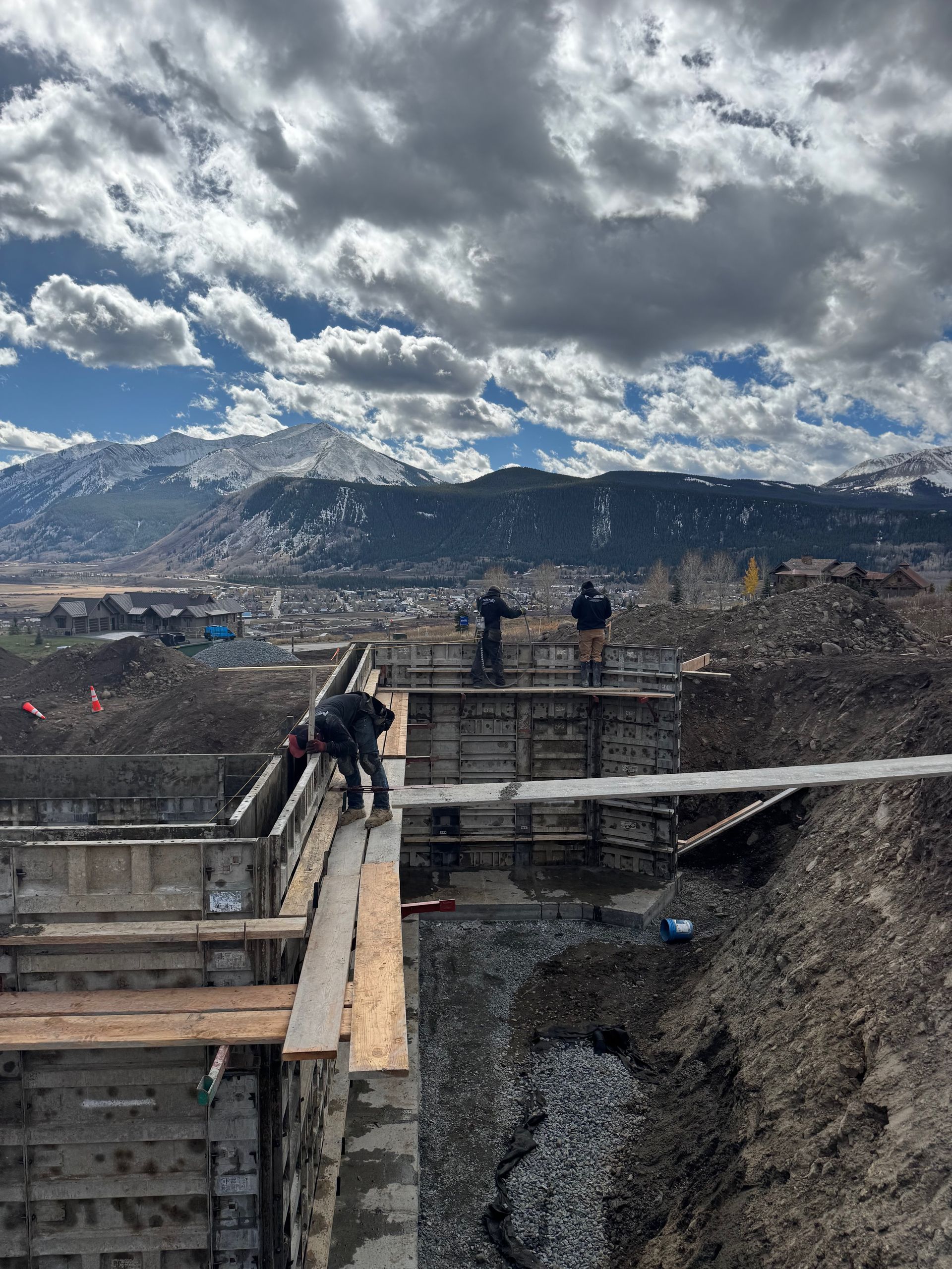Construction workers on wooden forms, mountains in background. Cloudy sky.