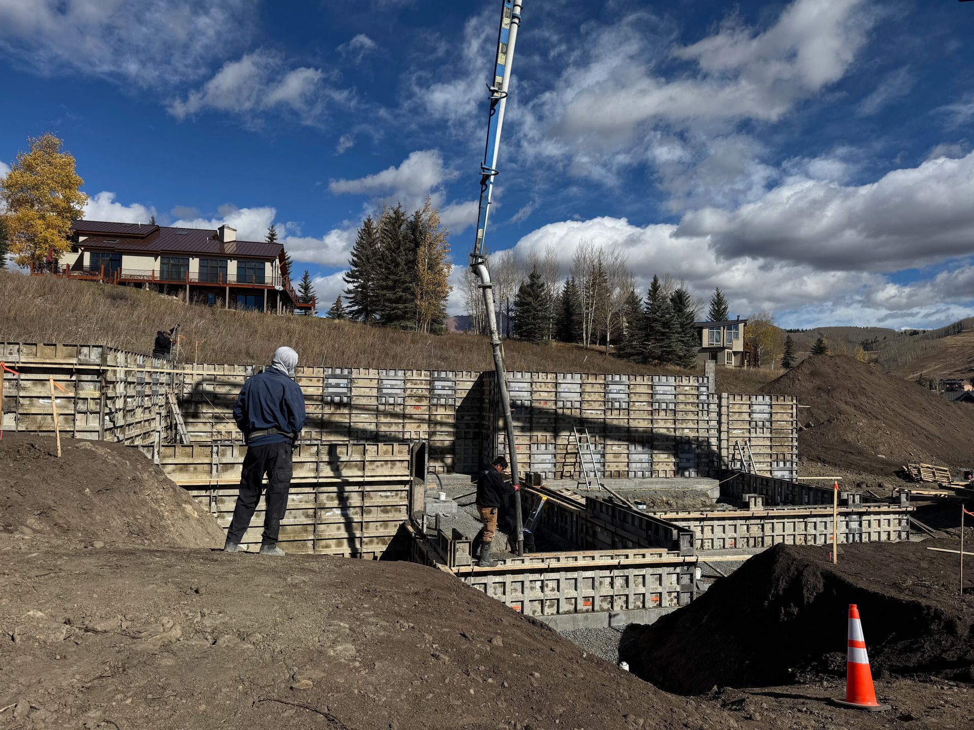 Construction site with concrete pouring. Man in hard hat observes concrete pump filling forms on a hillside.