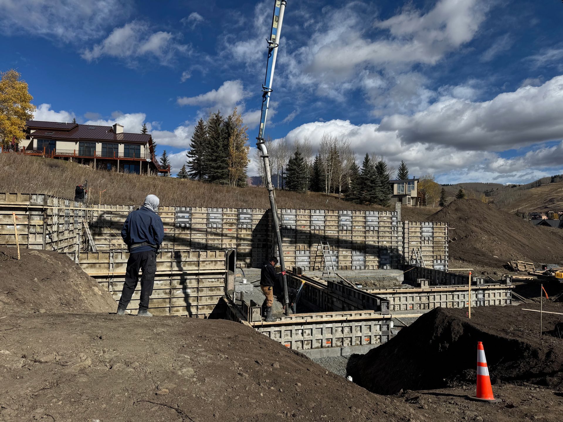 Construction site: workers pouring concrete into forms on a hillside under a blue sky.