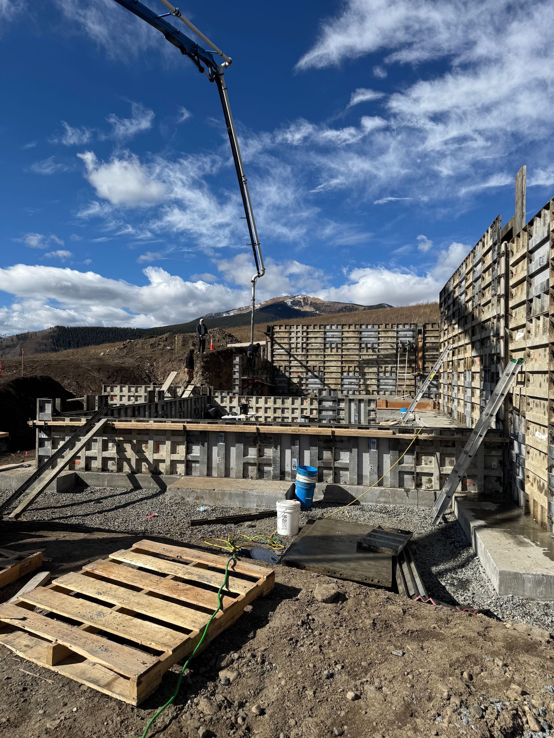 Construction site with concrete forms, a pump arm pouring concrete, and a mountain backdrop.