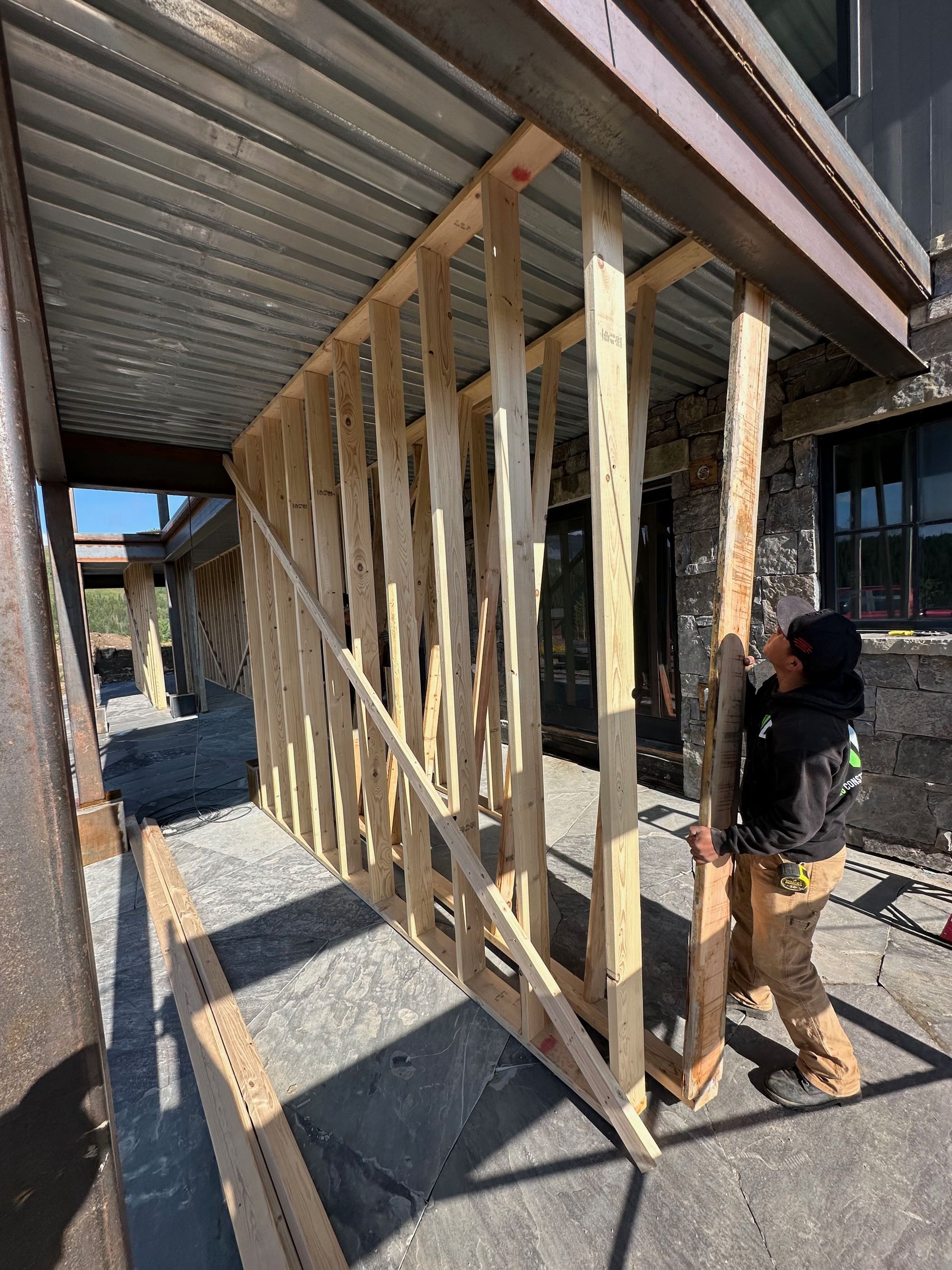 Construction worker framing a wall, outdoor setting, under a metal roof.