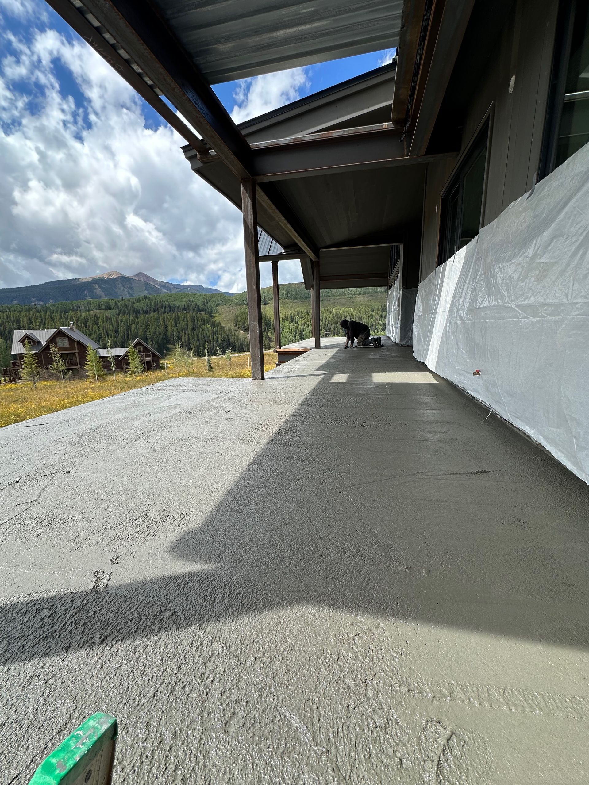 Exterior view of a building with a newly poured concrete walkway and gravel, under a shaded area; mountain background.