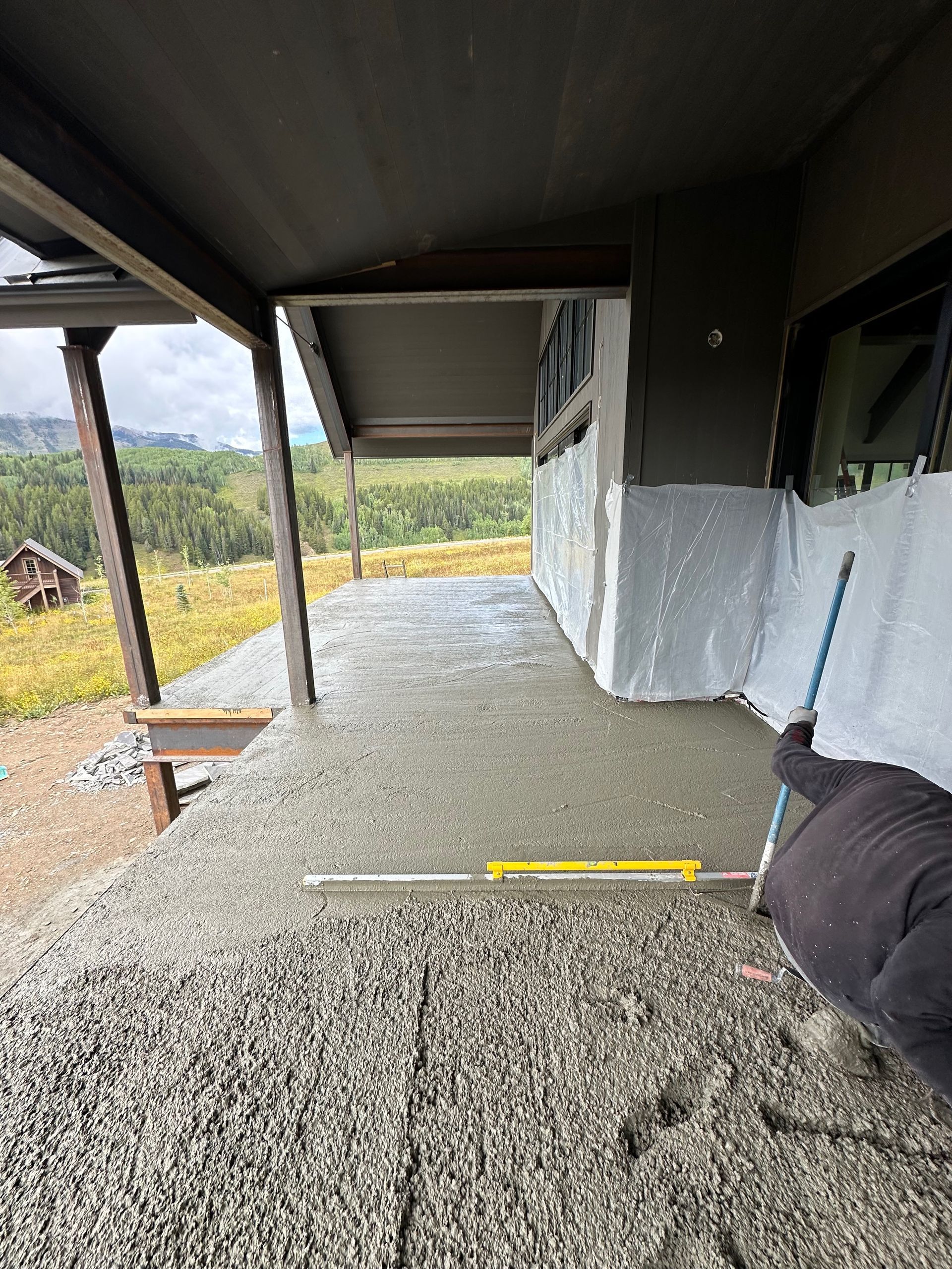 Concrete being leveled on a porch under a covered area; person holding a level, overlooking a hillside.
