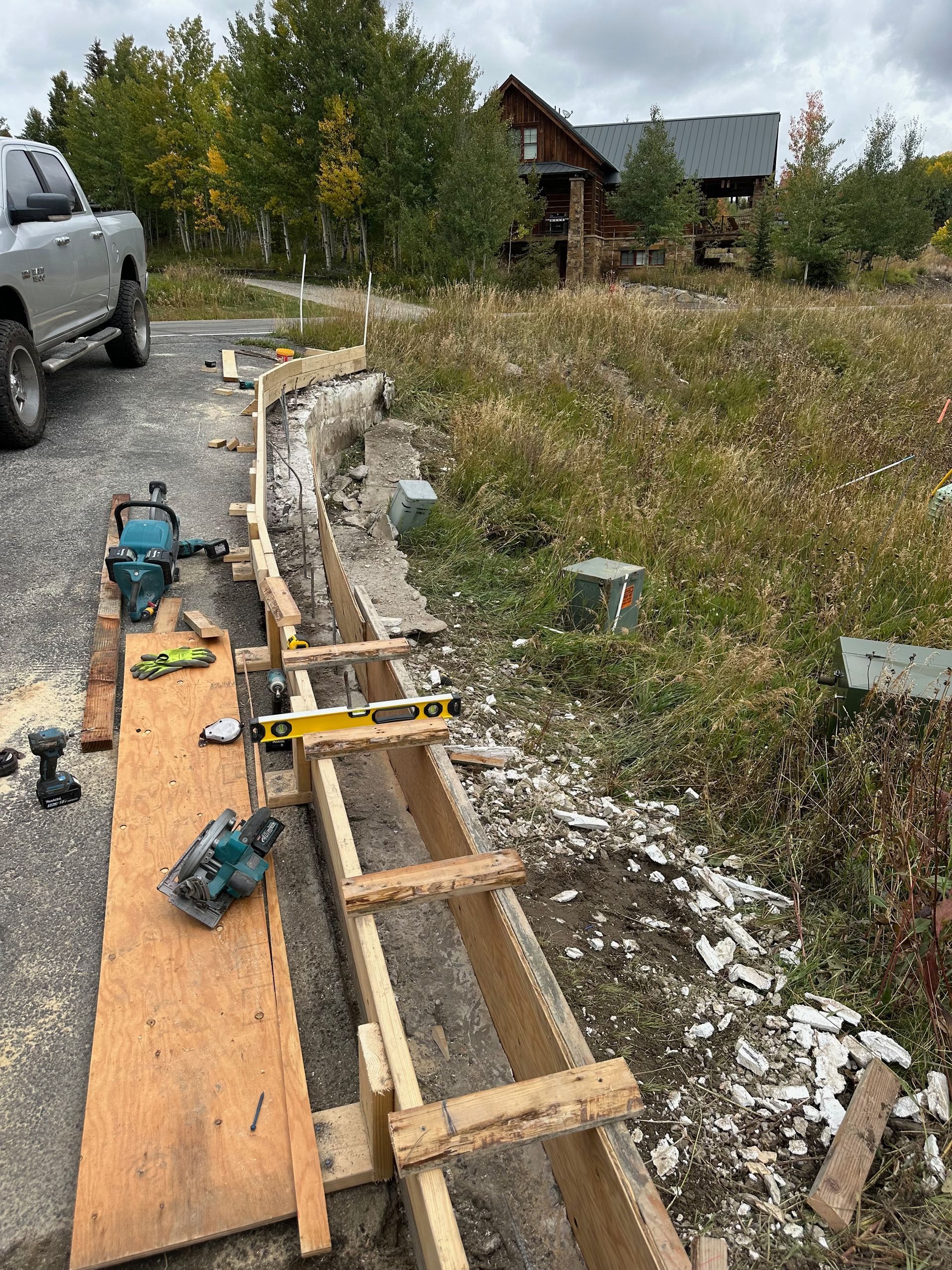 Construction site with wooden forms for concrete. Tools and a truck are visible, near a house.