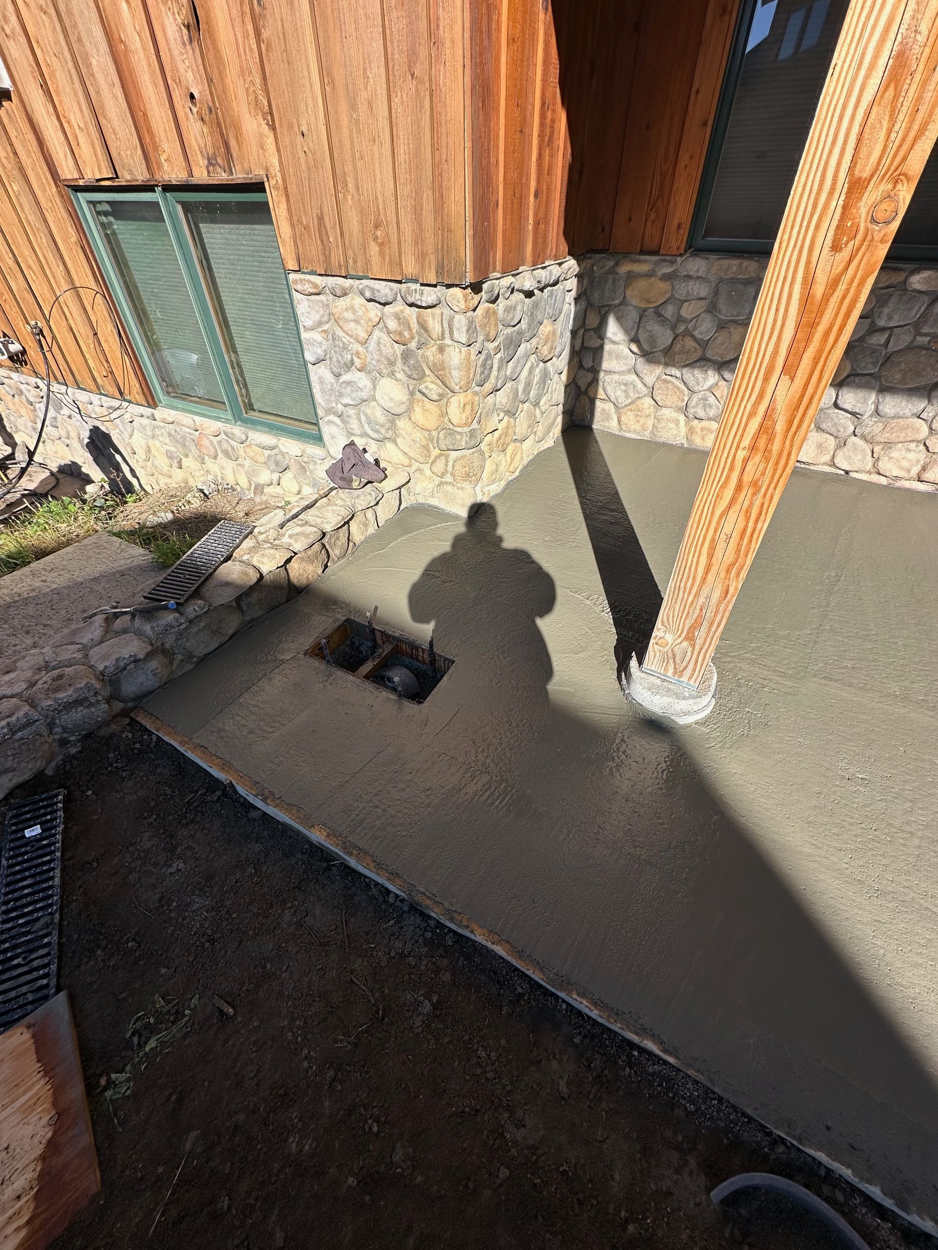 A person's shadow on a newly poured concrete patio near a wooden building.
