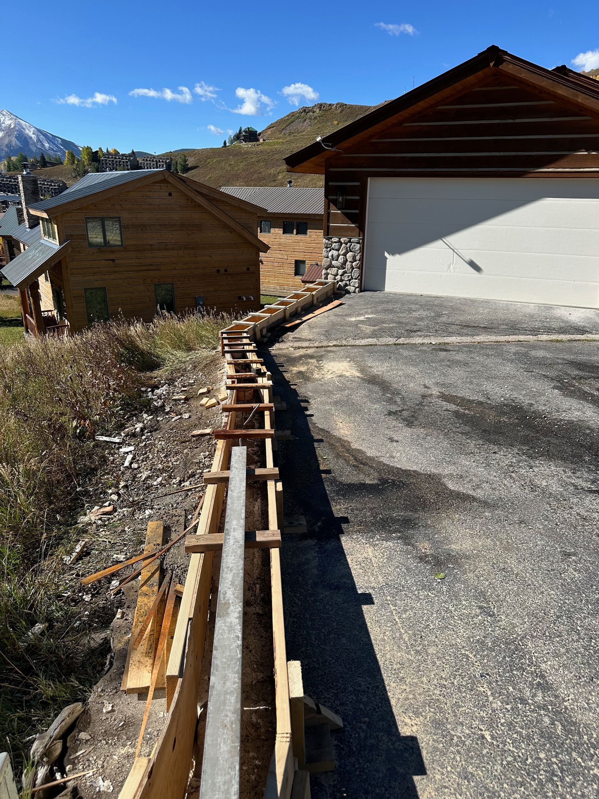 Wooden forms set for a concrete wall along a driveway in a mountain village setting.