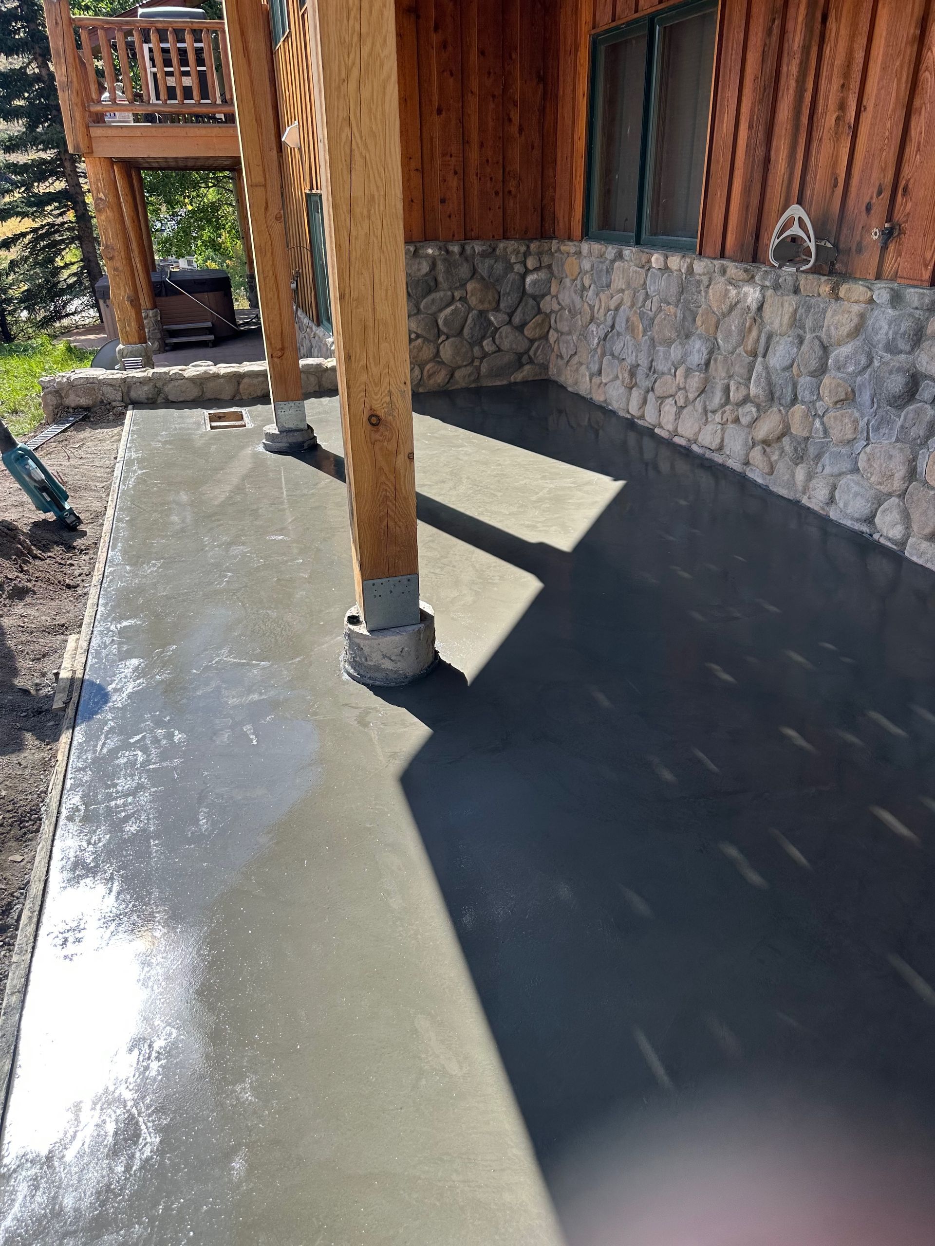 Exterior of a cabin with a freshly poured concrete patio; wood pillars, stone wall.