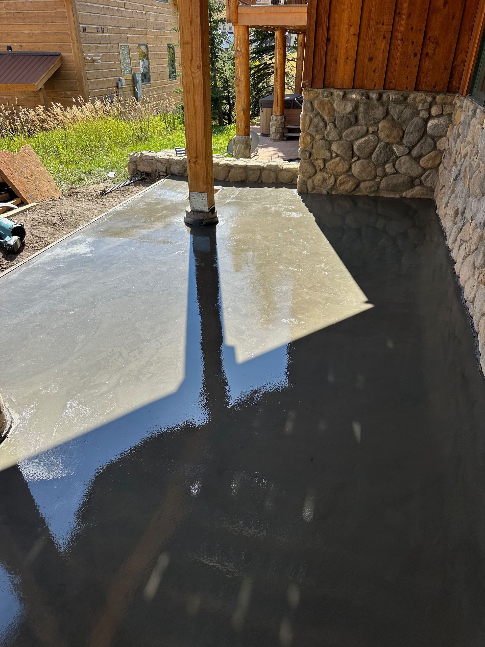 Newly poured concrete patio, partially shaded by a wooden structure.
