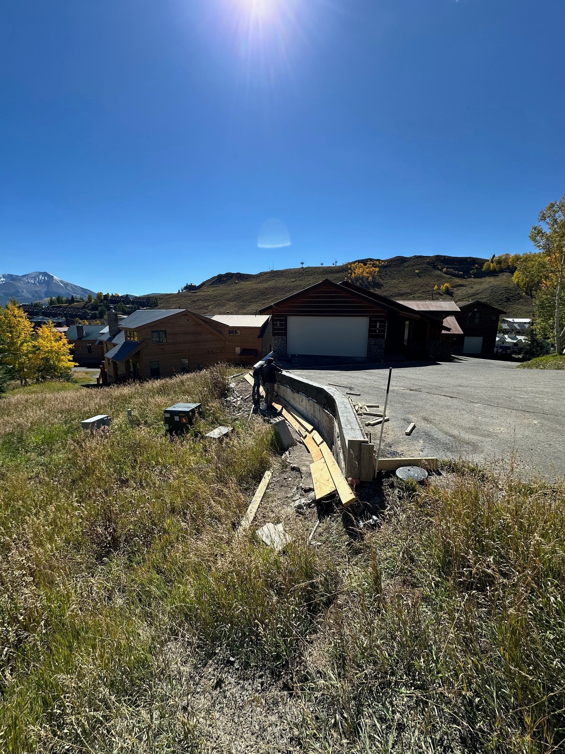A person stands near a curved construction project with a garage and building in the background on a sunny day.
