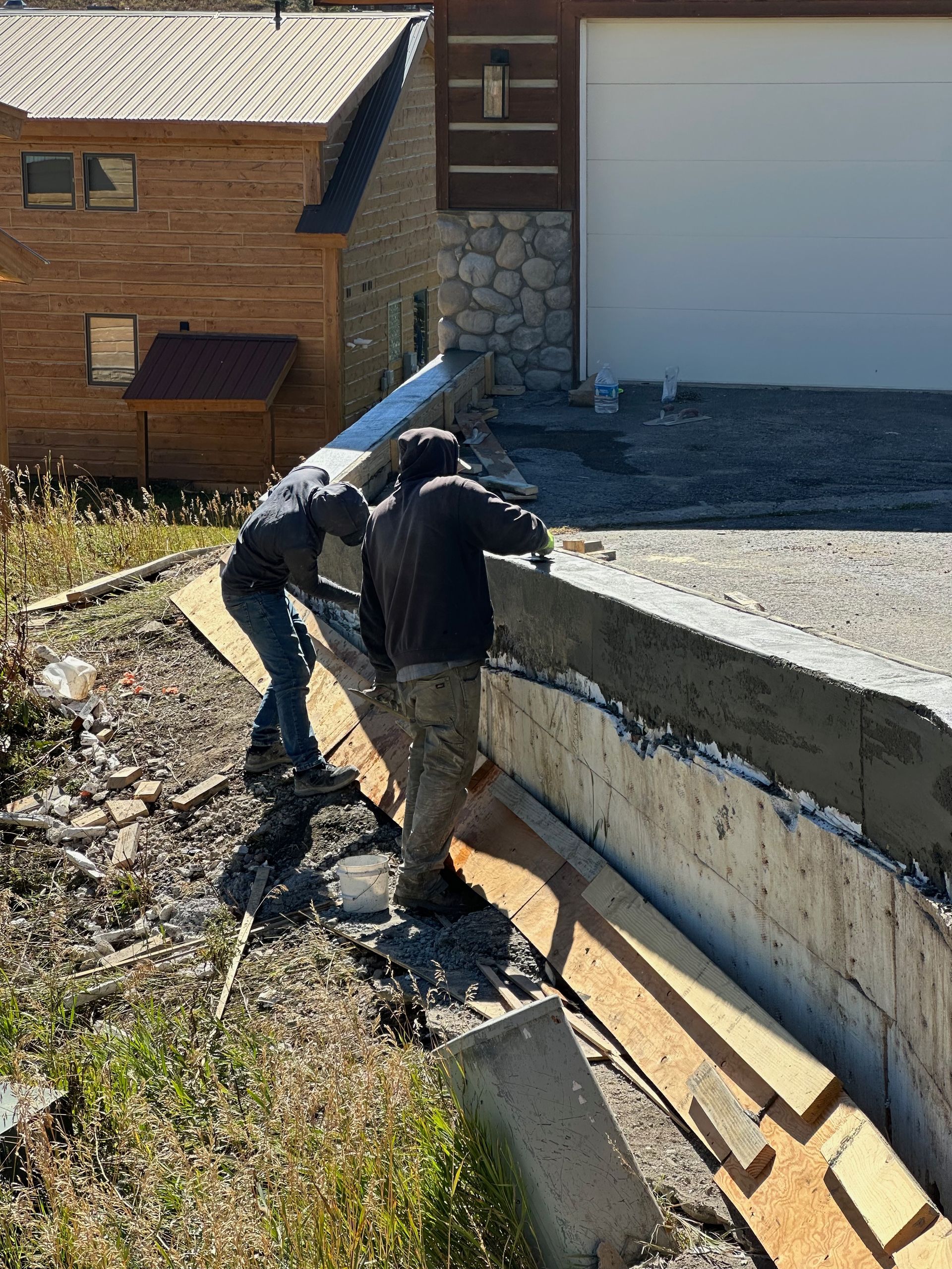 Two people working on a concrete wall outside a building with a garage door.
